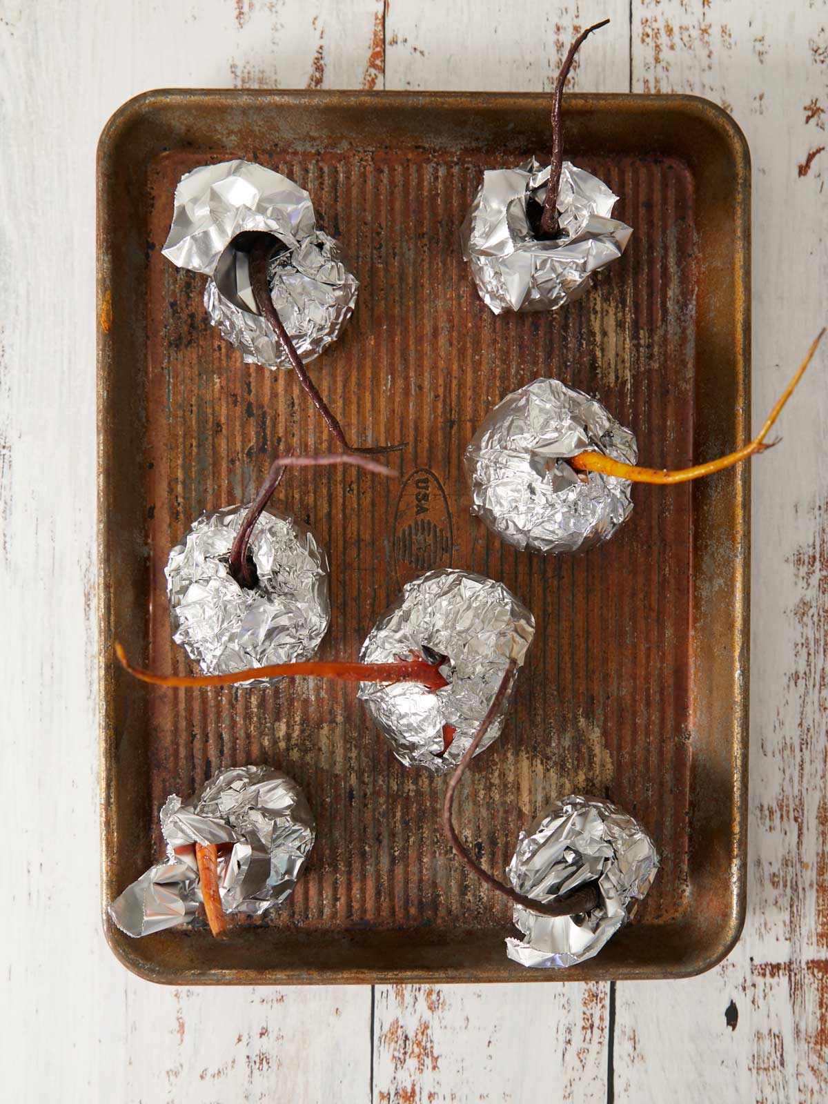 Seven beets individually foil wrapped on a sheet pan.