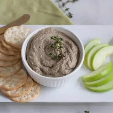 A bowl of hummus with crackers and apples.
