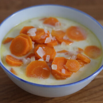 A bowl of soup with carrots in it.