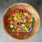A wooden bowl filled with corn, tomatoes and onions.