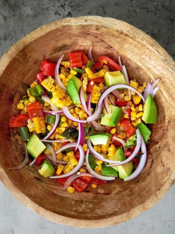 A wooden bowl filled with corn, tomatoes and onions.