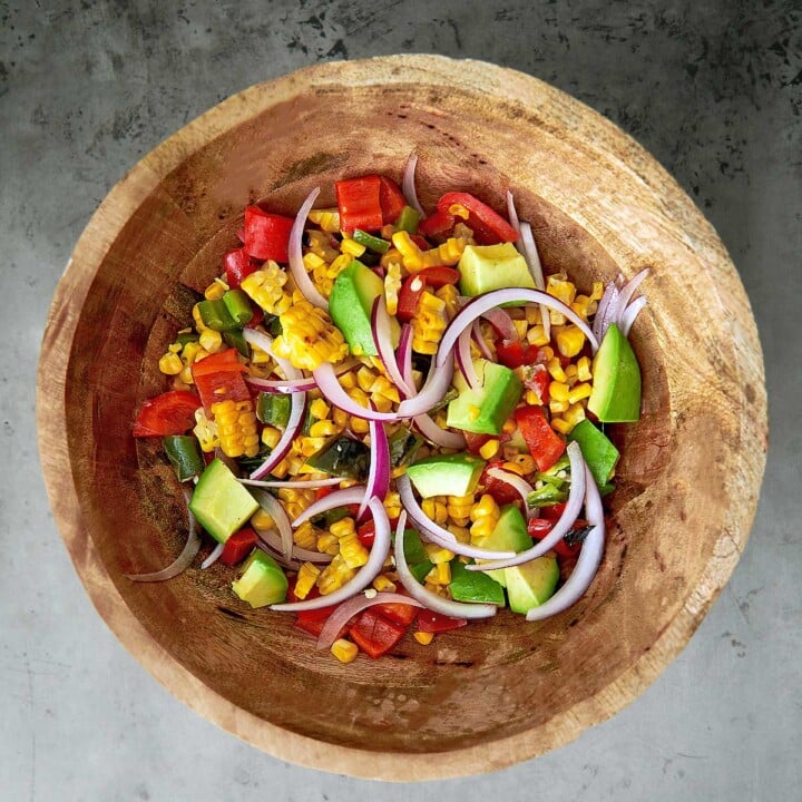 A wooden bowl filled with corn, tomatoes and onions.