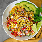 A bowl of corn salad with avocado and lime.