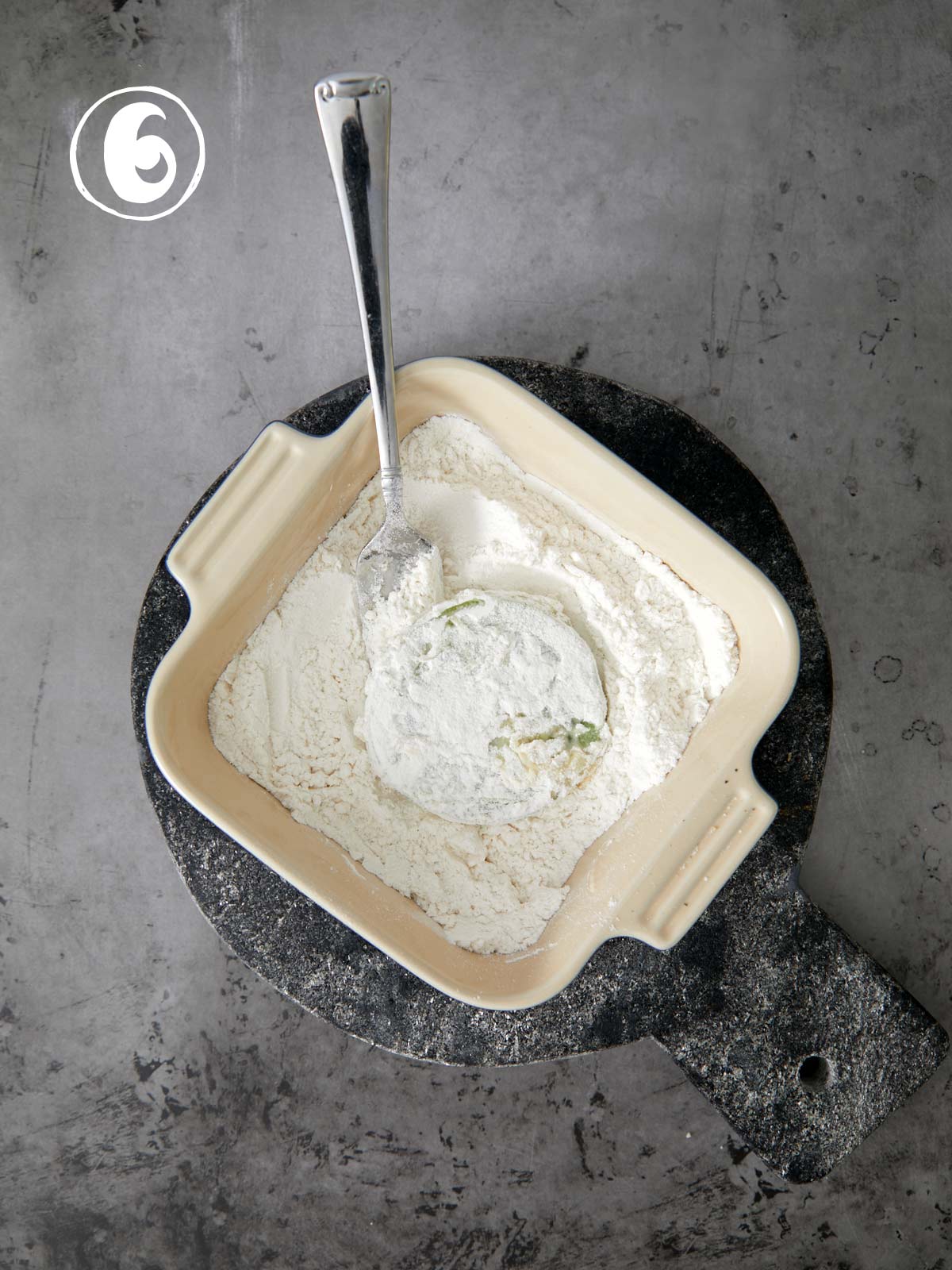 A bowl of flour with a green tomato and fork in it.