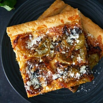 A square pizza with cheese and parmesan on a black plate.