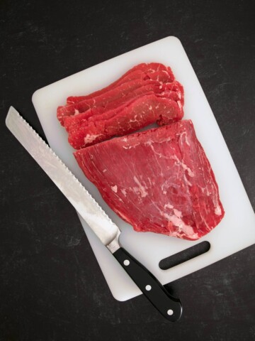 A piece of steak on a cutting board with a knife.