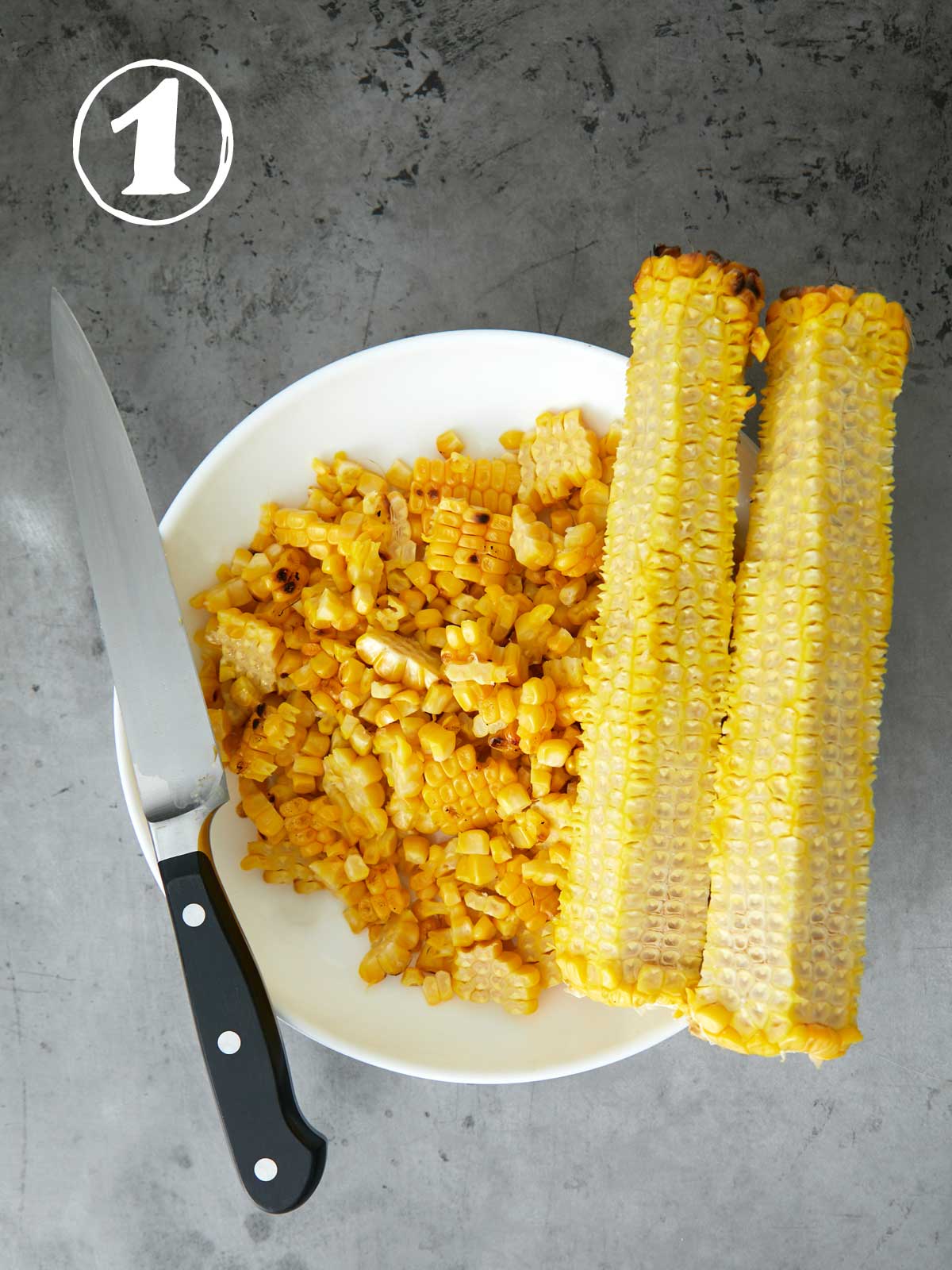 Corn on the cob on a plate with a knife.