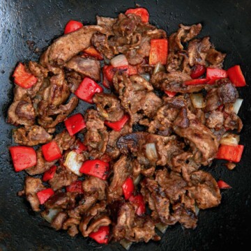 A wok with meat and peppers in it.