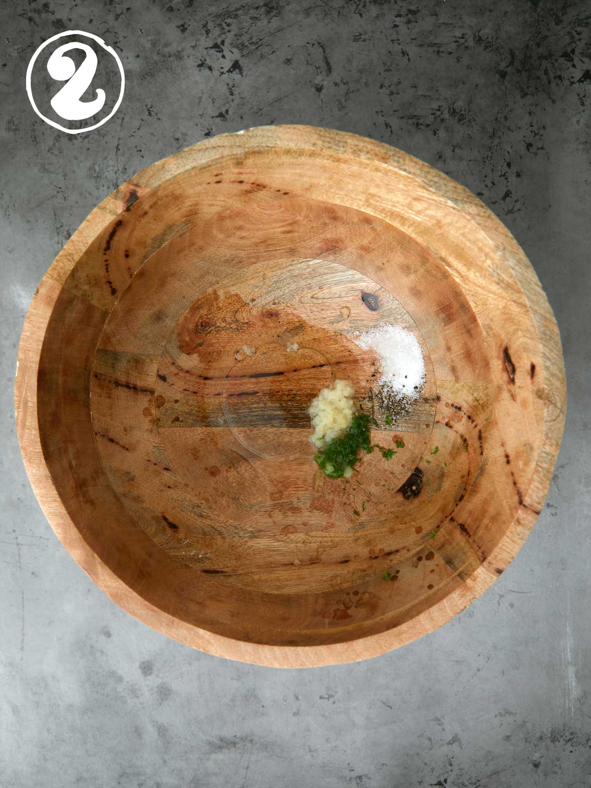 A wooden bowl on a concrete table with lime zest in it and garlic..