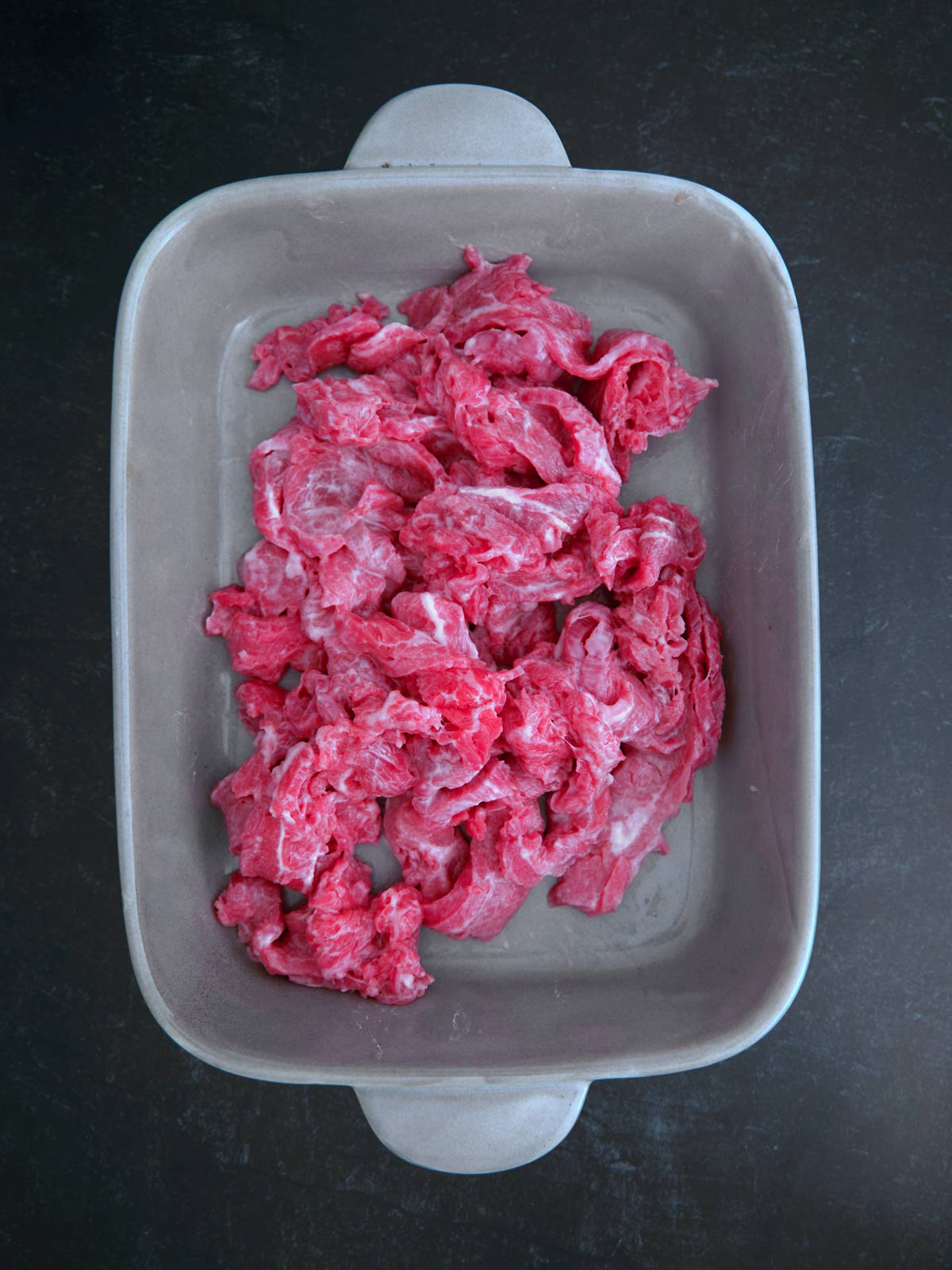 Red meat in a square dish on a black surface.