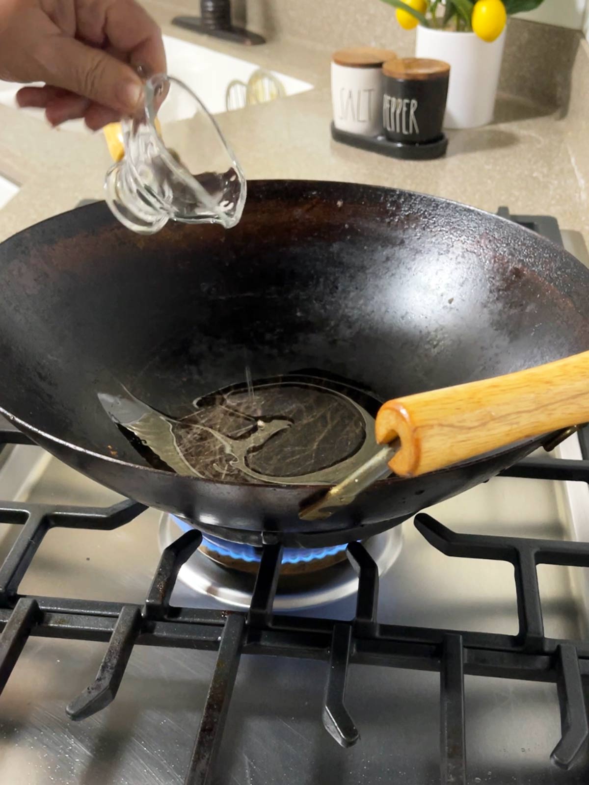 A person pouring oil into a wok on a stove.