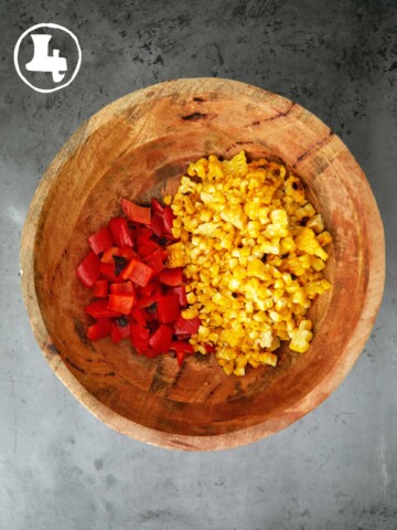 A wooden bowl filled with red peppers and corn.