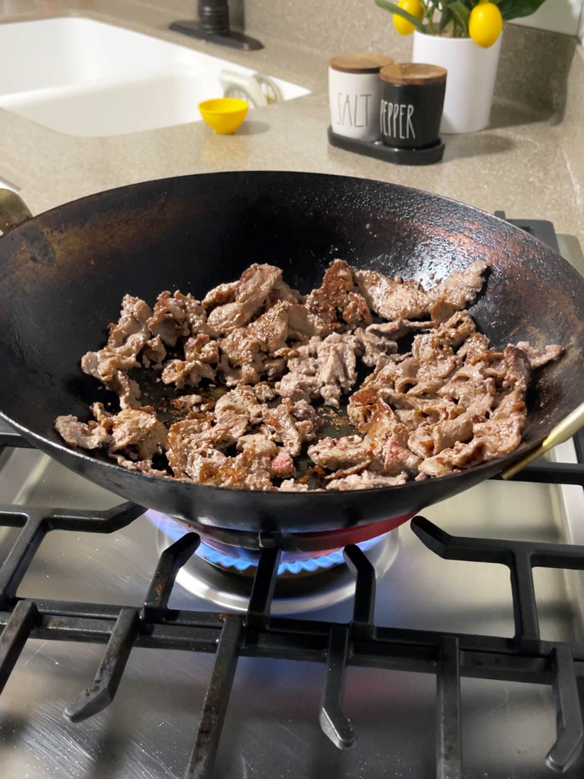 A wok on a stove with meat in it.