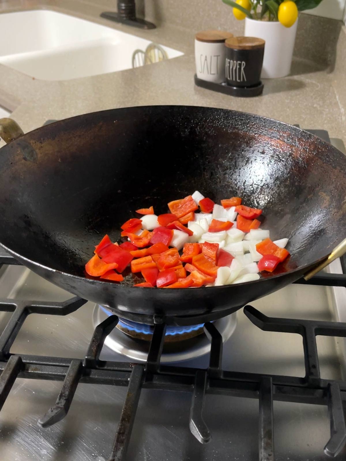 A wok filled with peppers and onions on a stove top.