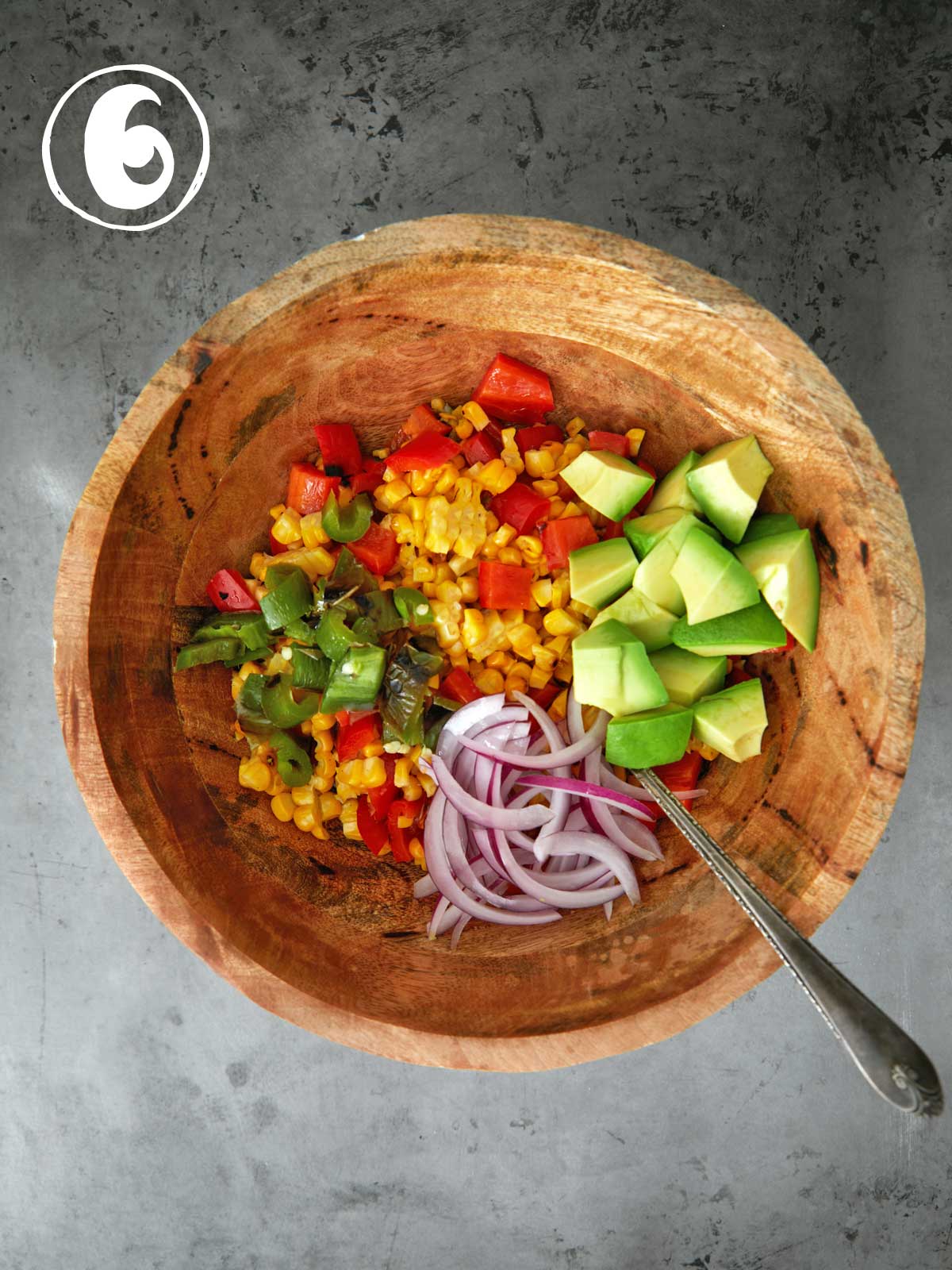 A wooden bowl with corn, tomatoes, onions and avocado.
