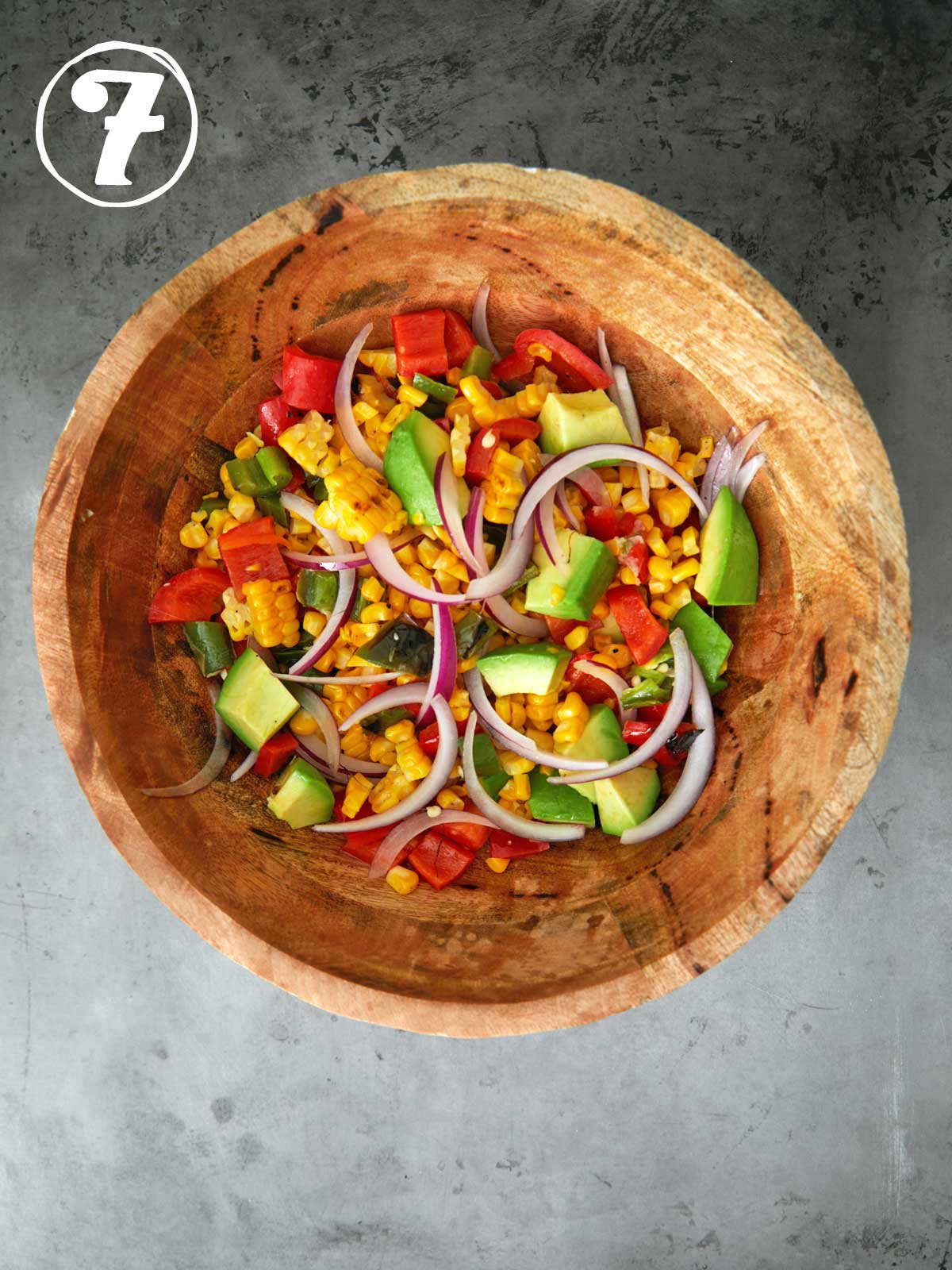 A wooden bowl filled with corn, tomatoes and onions.