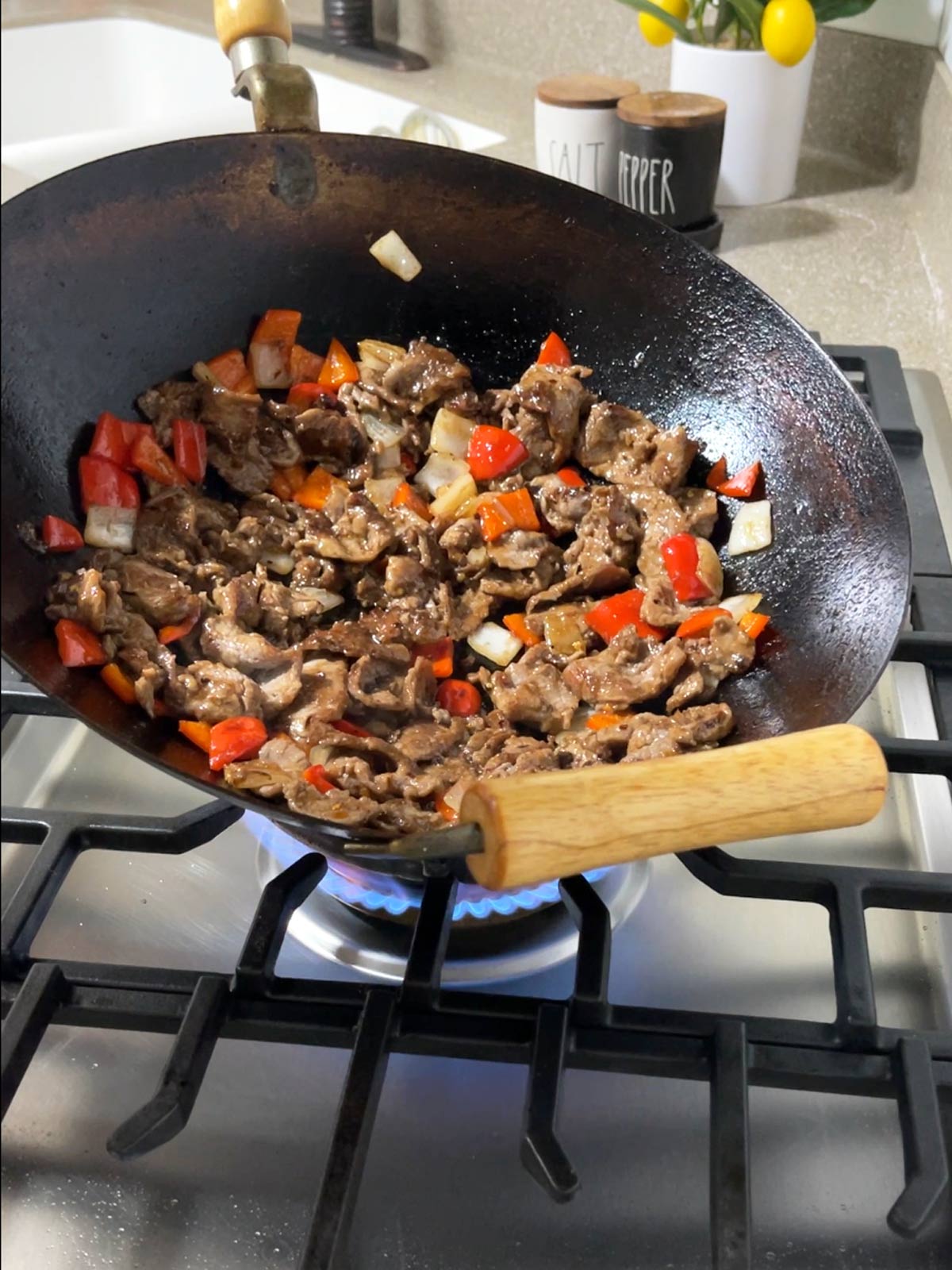 A wok with meat and vegetables cooking on a stove.