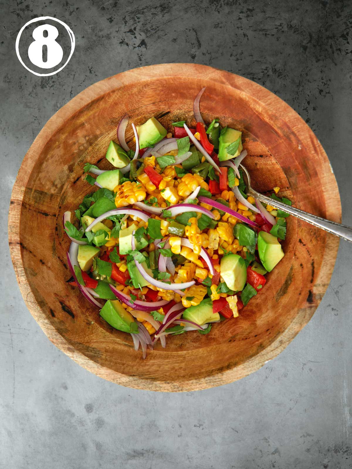 A wooden bowl with a salad with herbs on top in it.