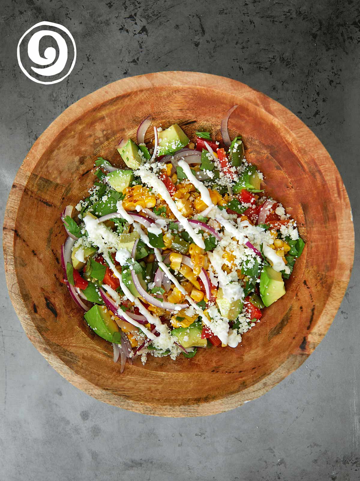 A wooden bowl with a salad in it with crema on top.