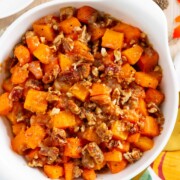 A white bowl filled with roasted butternut squash and sweet potatoes topped with chopped pecans.