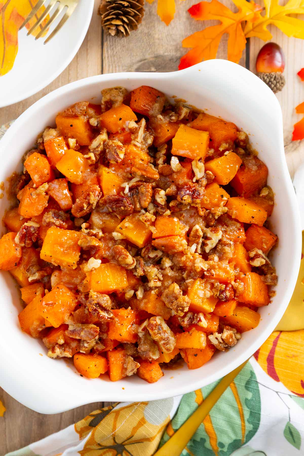 A white bowl filled with roasted butternut squash and sweet potatoes topped with chopped pecans.
