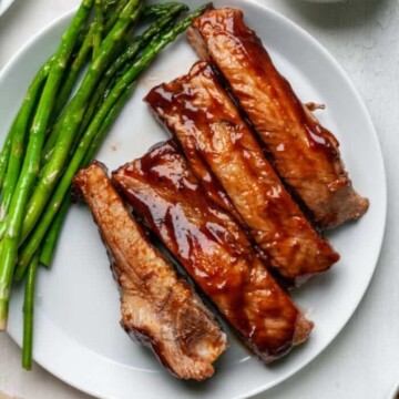 Bbq ribs on a plate with sauce and asparagus.
