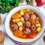 A bowl of soup with meatballs and vegetables.