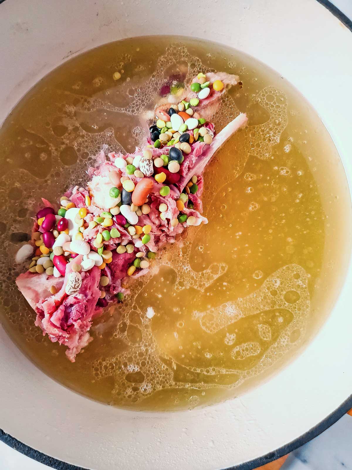 A pot of soup with meat and beans in it, featuring ham shank prepared in pot.