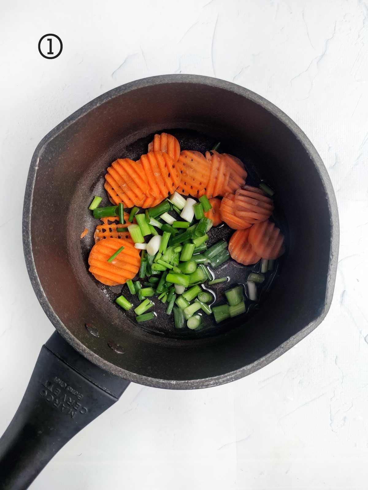 A frying pan with carrots and onions in it.