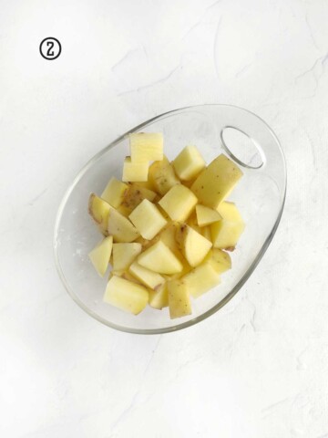 Sliced potatoes in a glass bowl on a white surface.