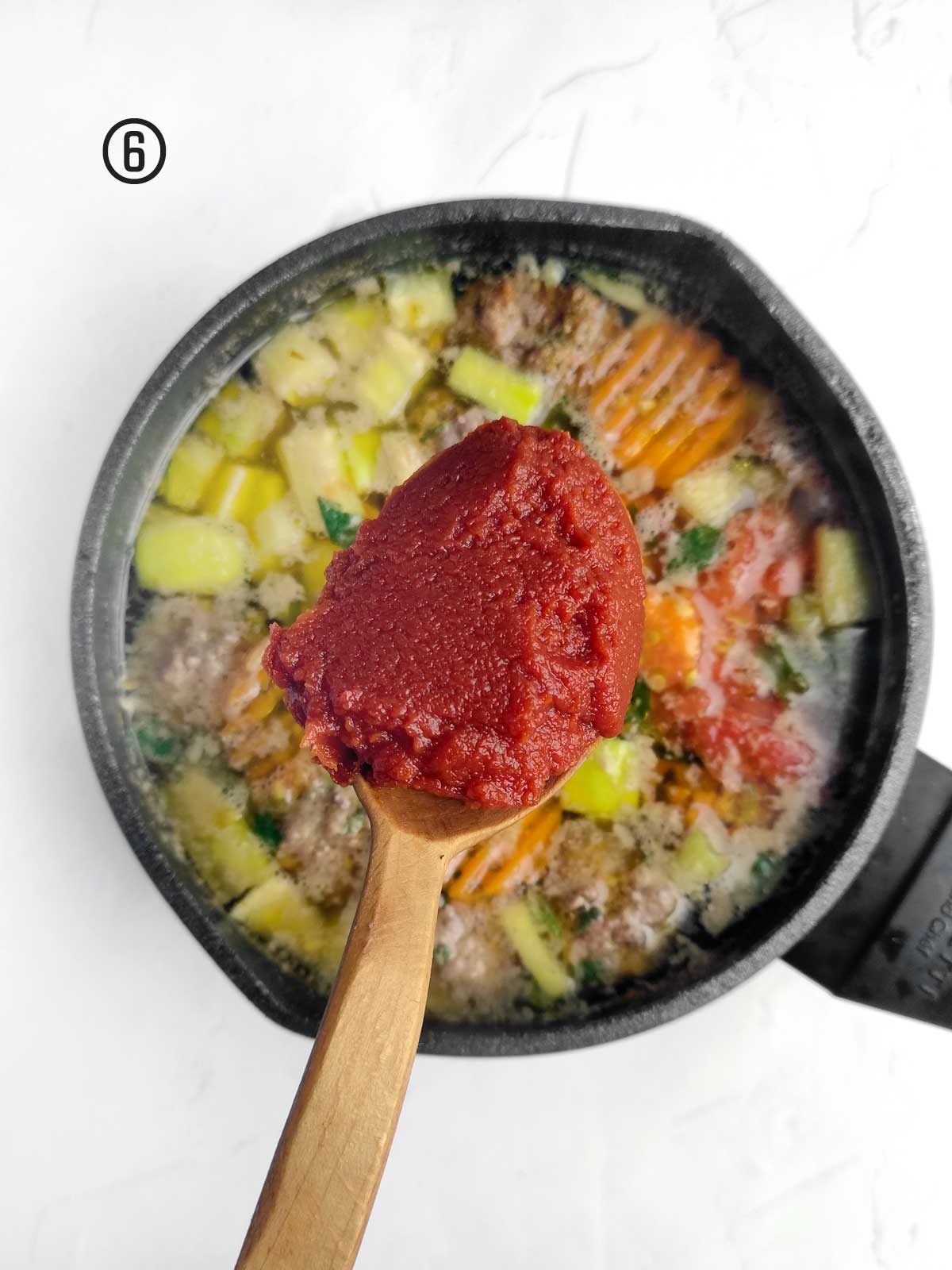 A wooden spoon is being used to stir a red sauce in a pan.