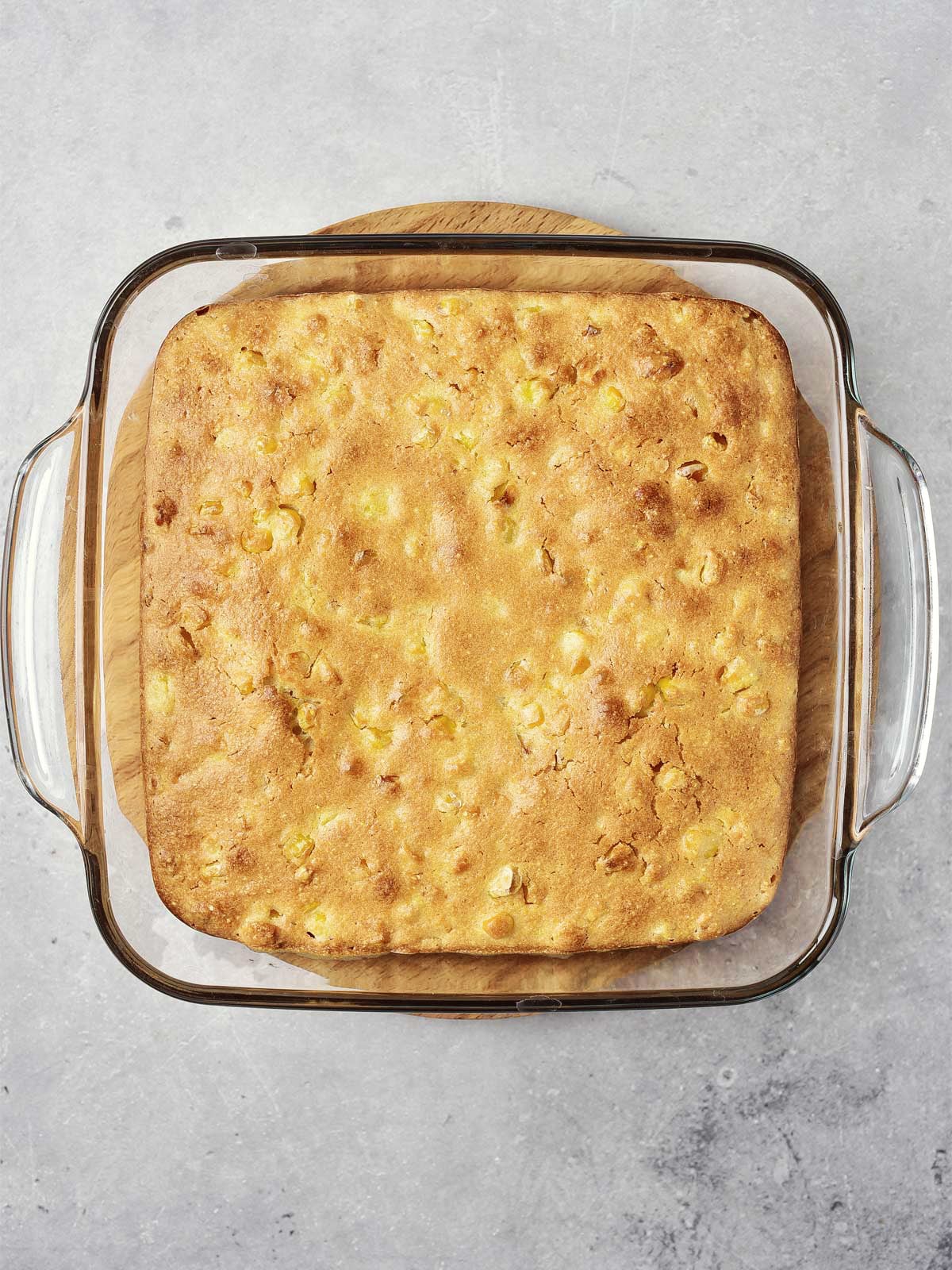 A square pan of golden-brown baked cornbread resting on a wooden board, perfect for an easy corn casserole without creamed corn.
