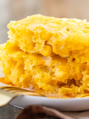 Two stacked squares of easy corn casserole served on a white plate with a gold fork.