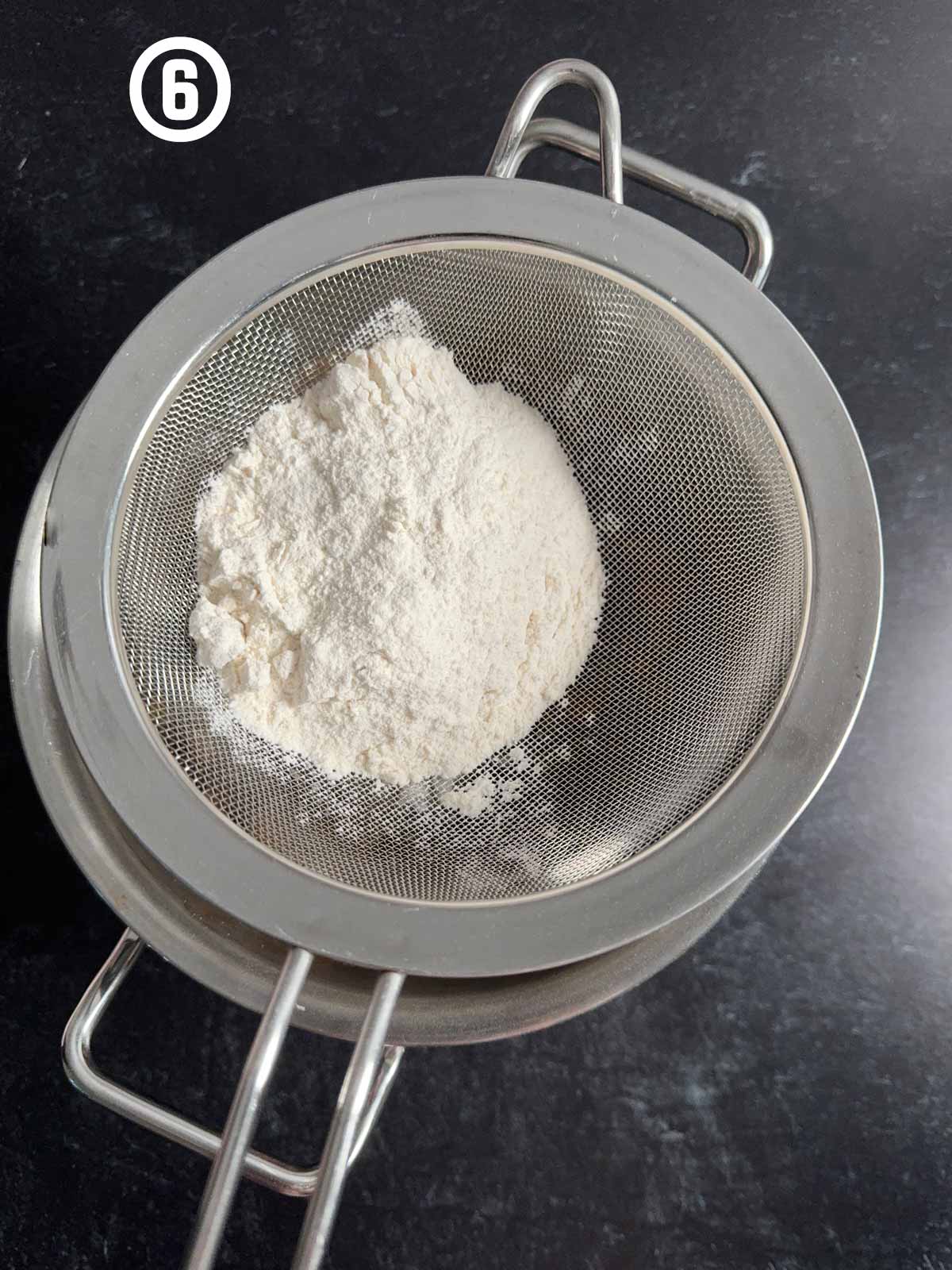 Flour in a metal strainer on a table.