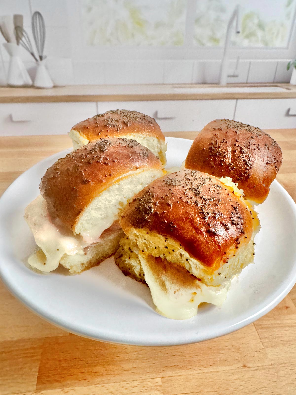 A plate with four delicious ham and cheese sliders on it.