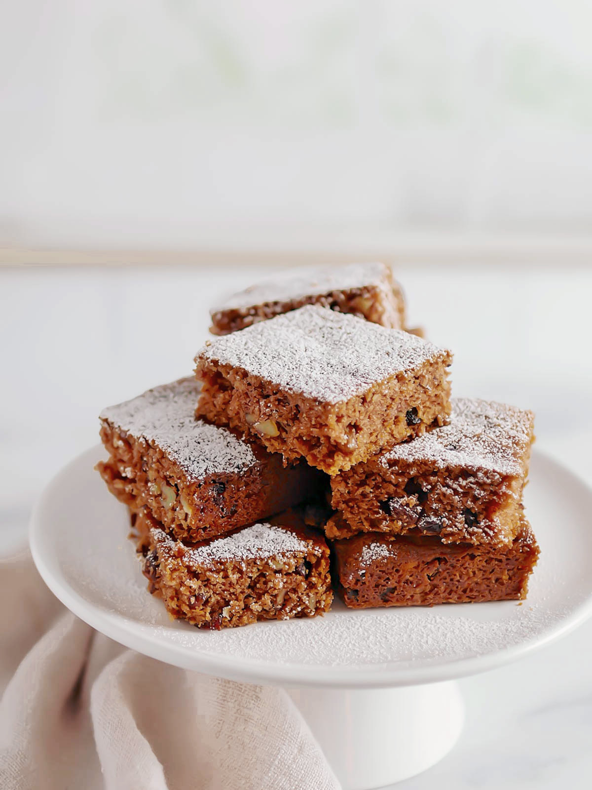 A white plate with a stack of delicious spice cake  squares on it, including powdered sugar topping.