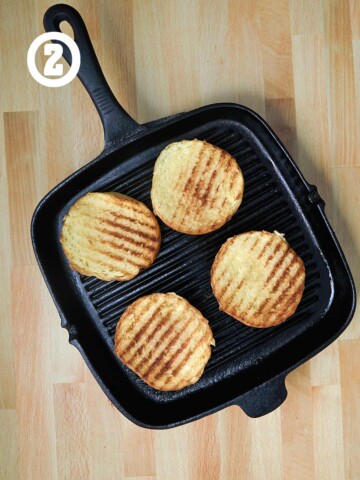 A grill pan with toasted hamburger buns on a wooden table.