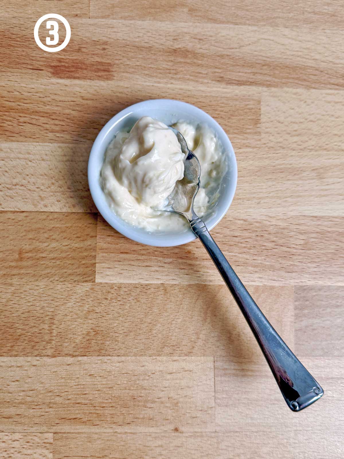 A bowl of mayonnaise mixture with a spoon on a wooden table.