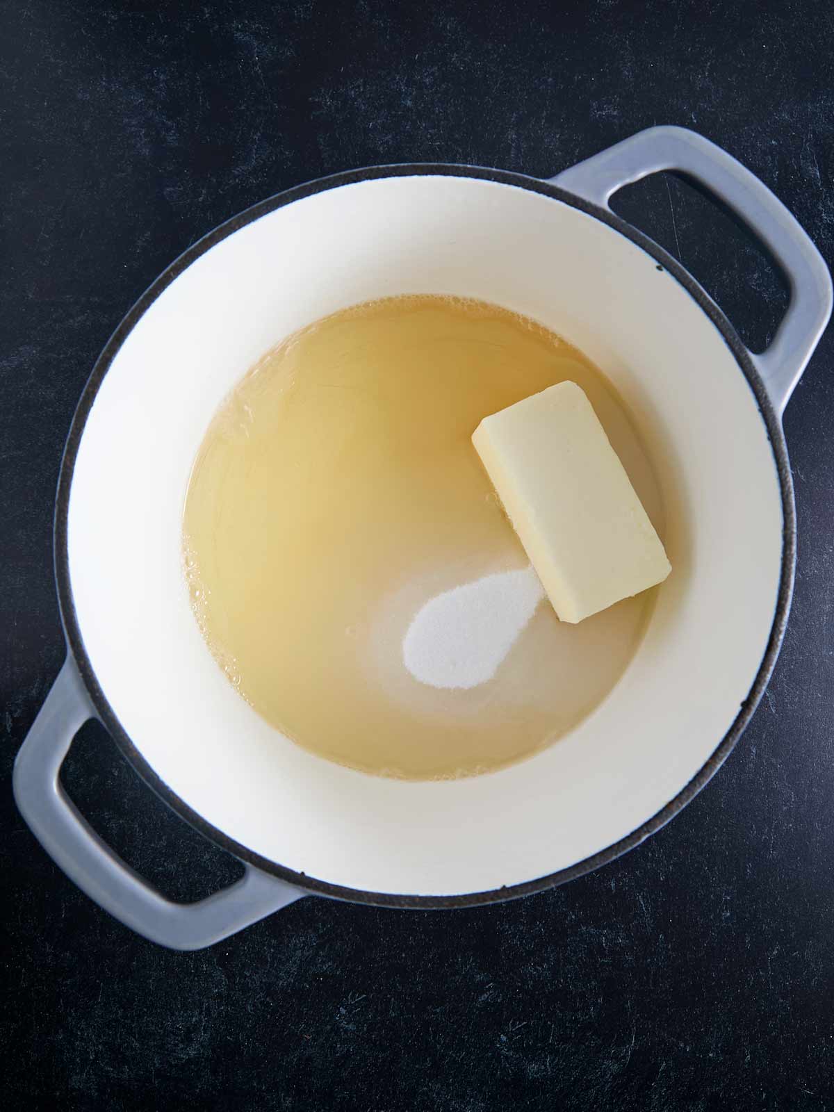 A pot with Irish whiskey, sugar, and butter in it on a black surface.