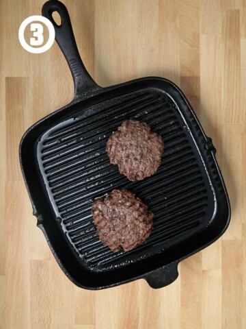 Two burgers in a cast iron grill pan.