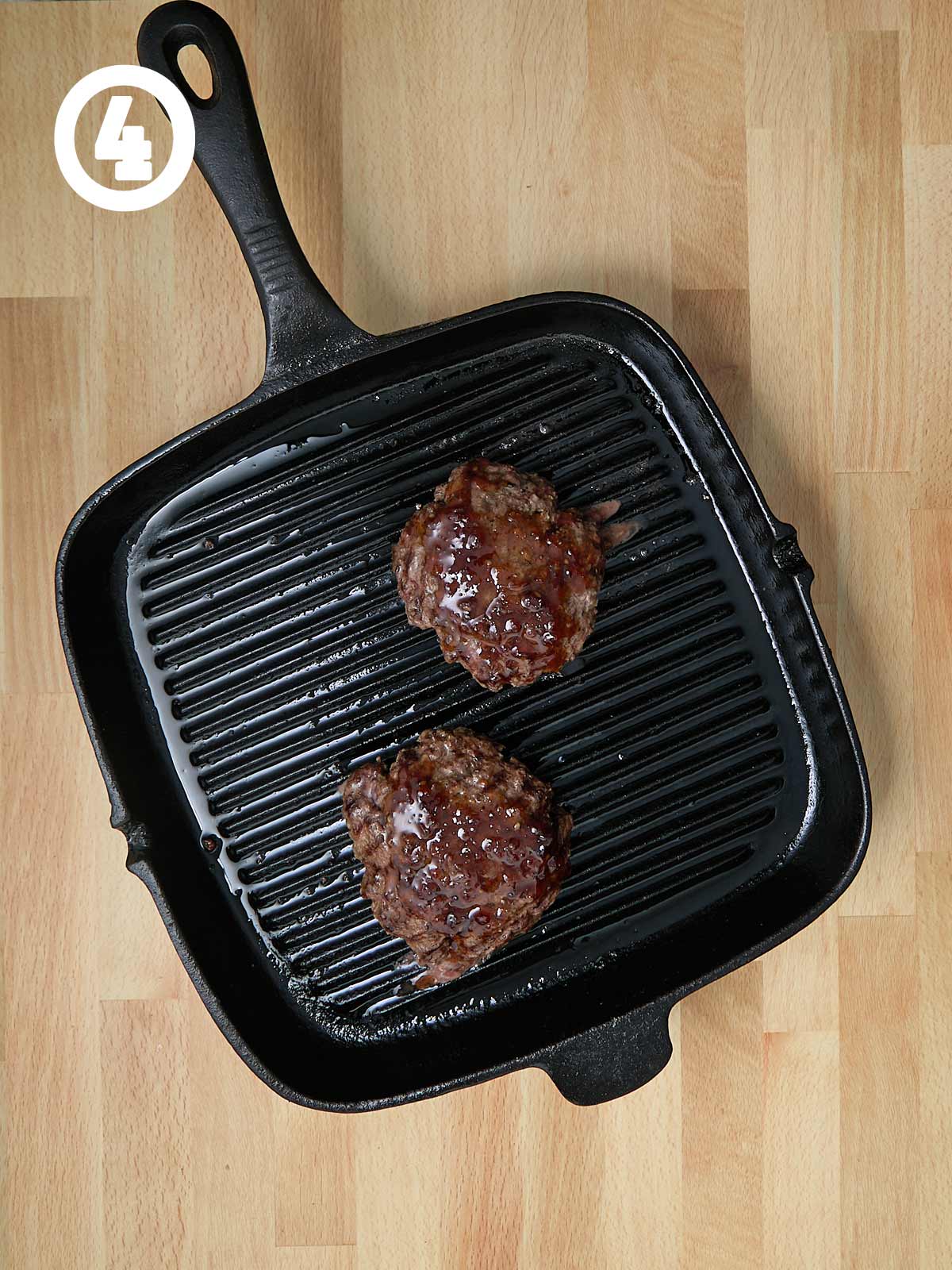 Two burgers with Jack Daniels sauce in a cast iron grill pan.