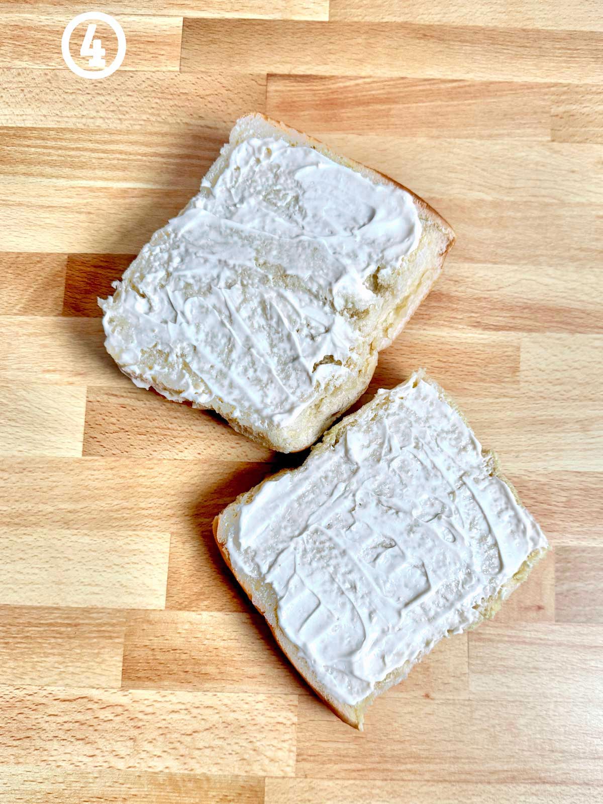 Two slices of bread on a wooden table, with mayonnaise/horseradish spread.