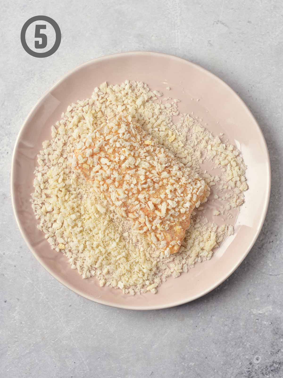 A plate with panko bread crumbs and fish on a white surface.