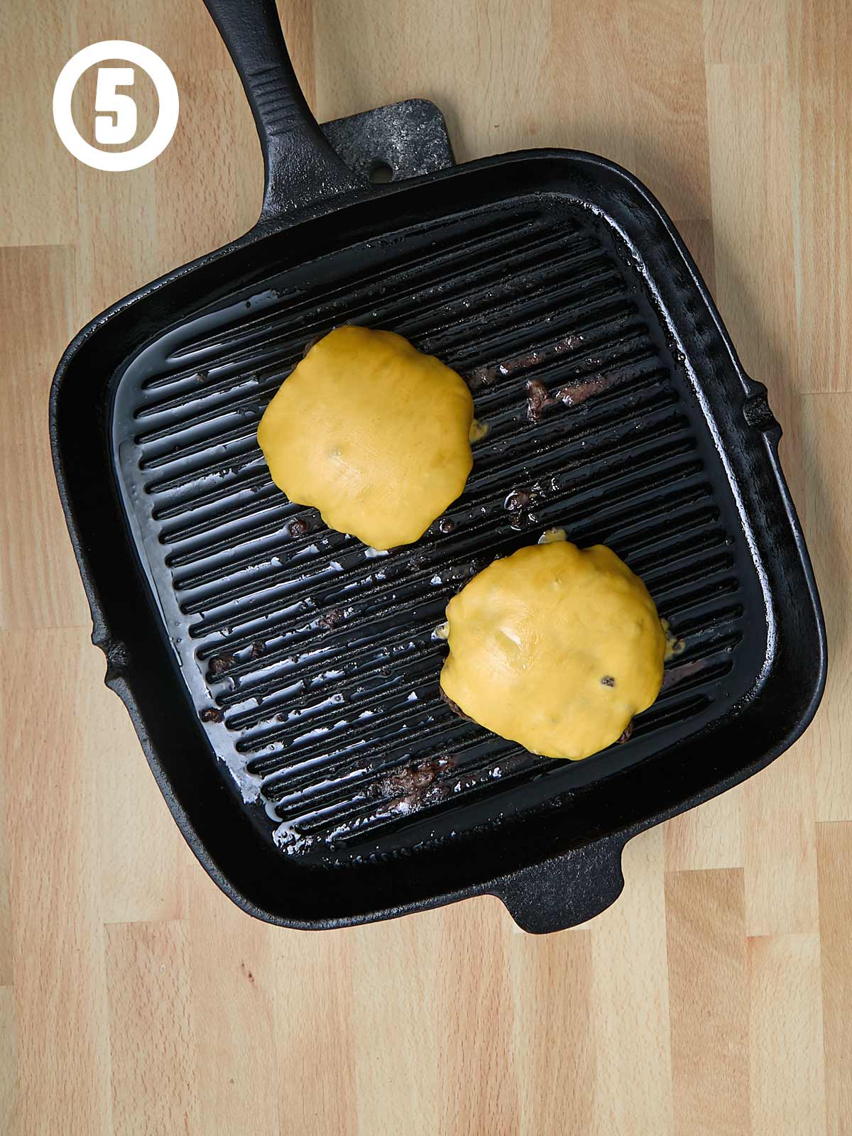 A grill pan with two burgers with melted cheese in it.