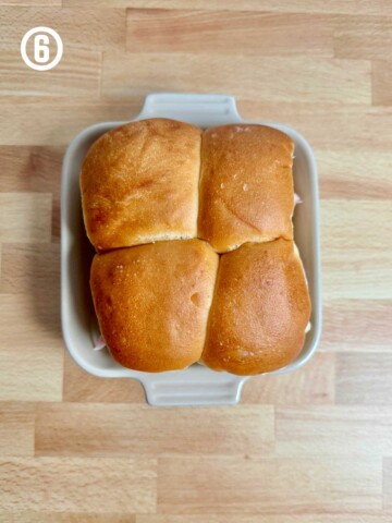 Ham and cheese sliders in a white dish on a wooden table.
