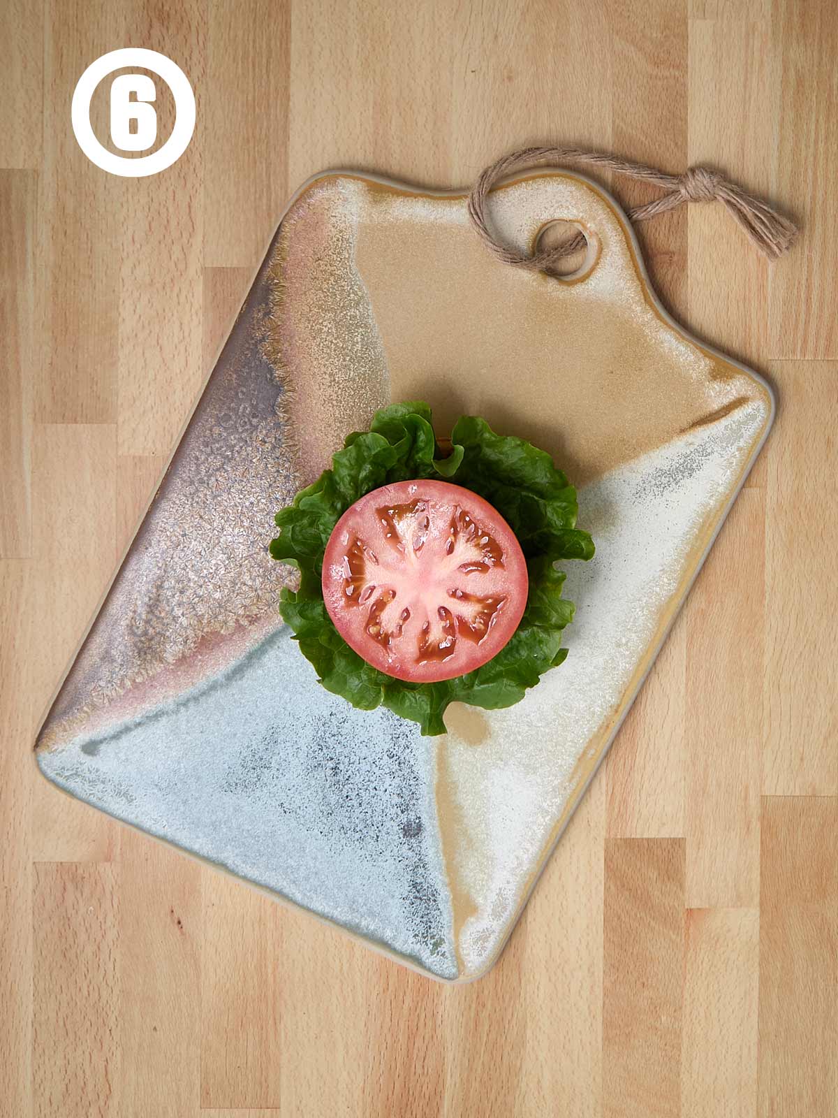 A wooden cutting board with a burger bun, lettuce, onion, and tomato on it.