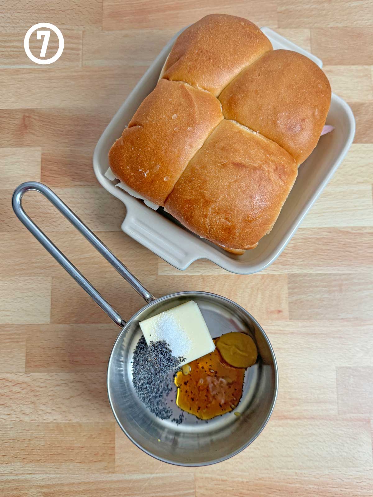 A pan with a loaf of bread next to a measuring cup with honey, butter, poppy seeds, salt, and mustard.