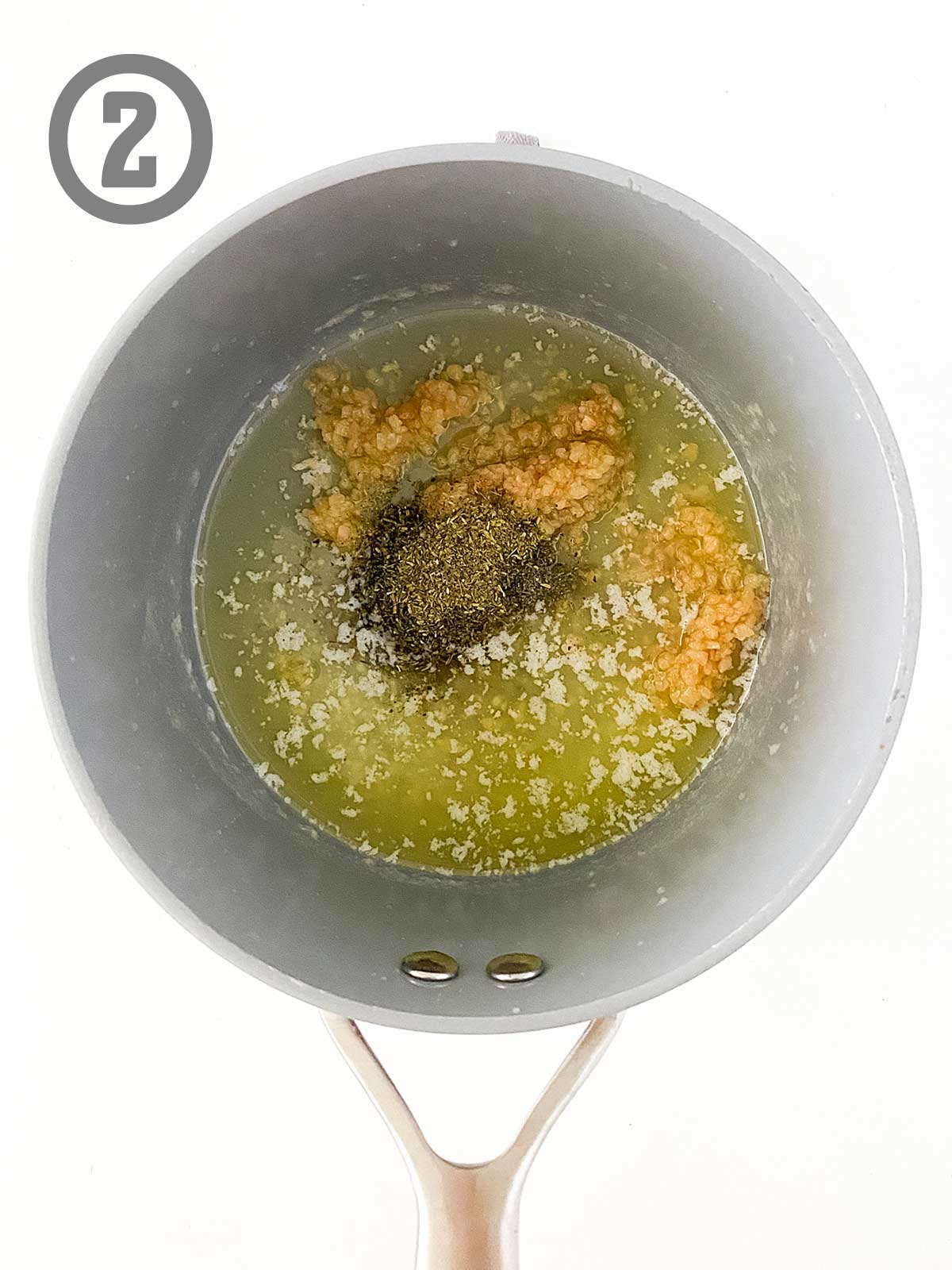A saucepan filled with a melted butter, garlic, and Italian seasoning.