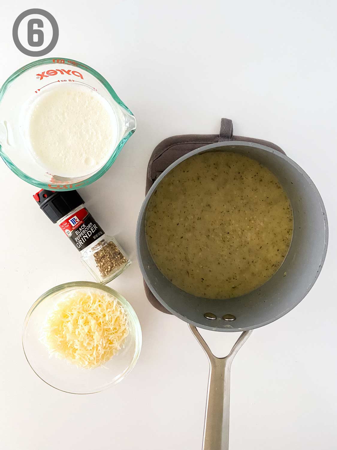 A saucepan with sauce and contianers of cheese, pepper, and heavy cream.