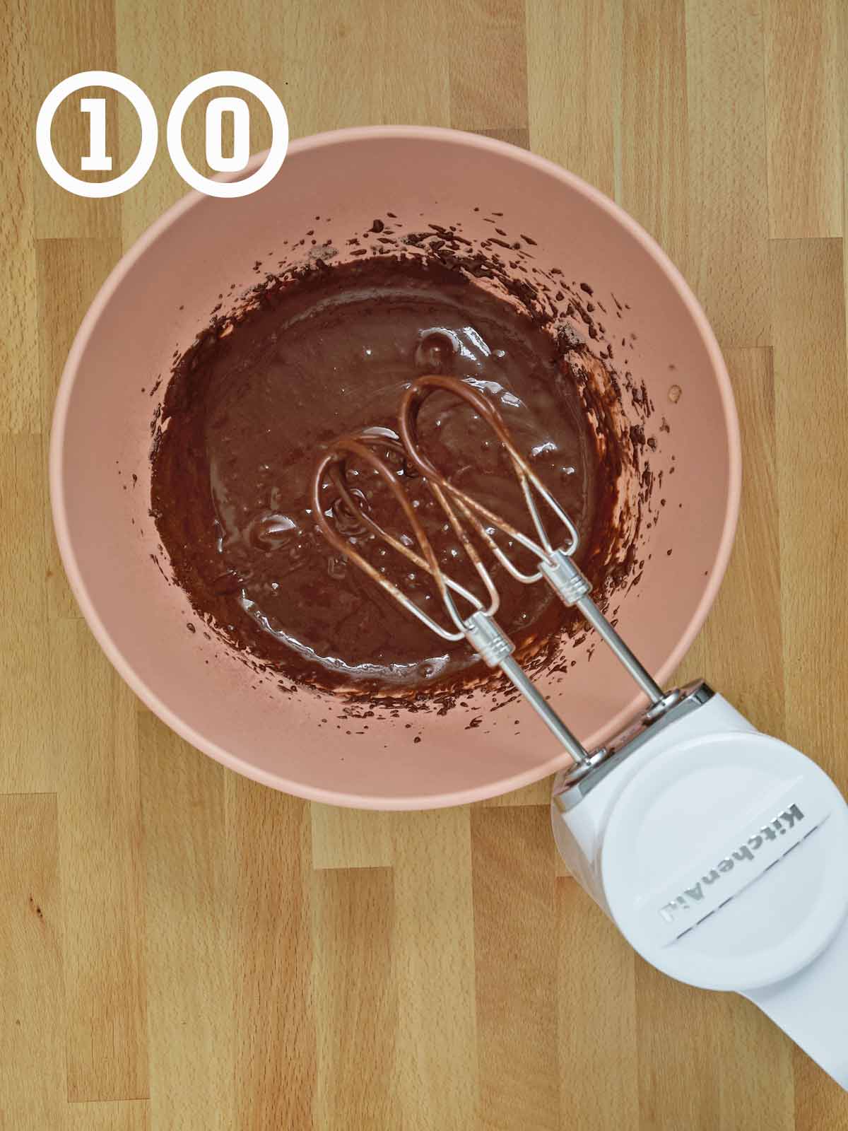 A bowl of chocolate cake batter with a mixer.